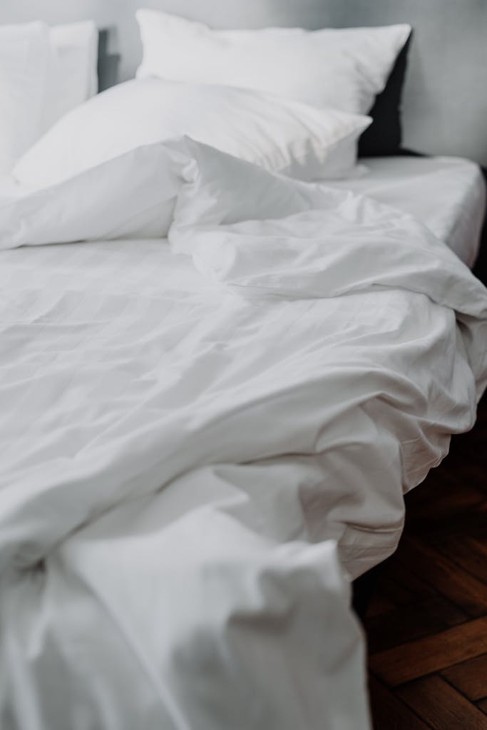 A close-up of a cozy white linen bed with rumpled bedding in a modern bedroom setting.